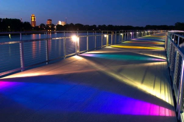 Pedestrian bridge at Gray's Lake lit up with colored lights at night.