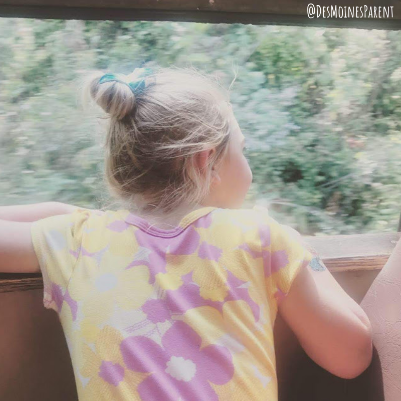 Girl leaning out the window of an open-air train car.