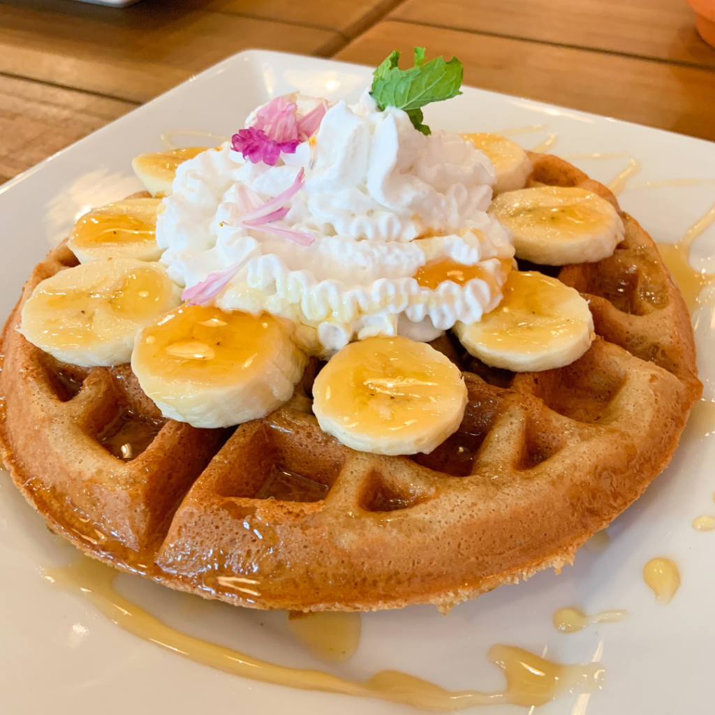 Waffle covered in bananas and whipped cream.