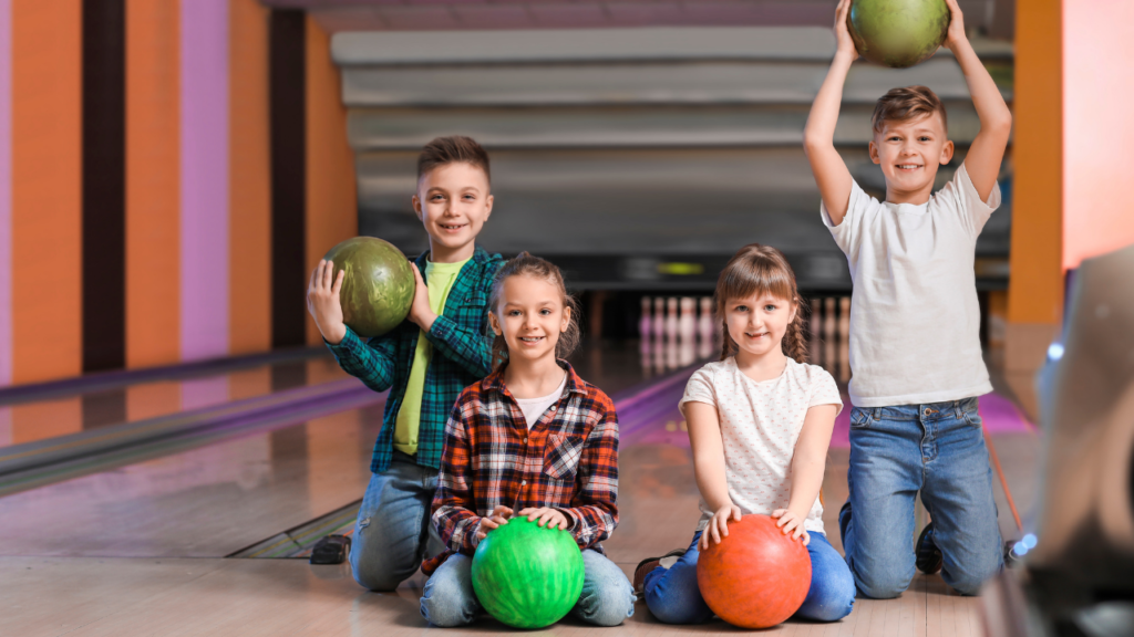 Four kids on a bowling alley holding bowling balls and smiling.